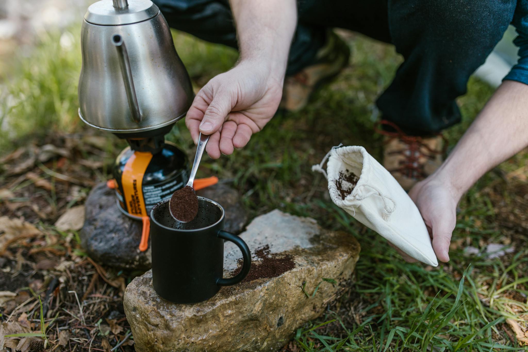 Person preparing coffee with portable kettle on a camping trip.